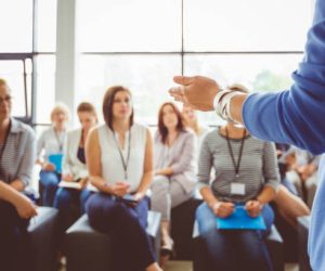 Hand of a trainer addressing group of females sitting in a conference hall. Female hand against defocused group of women attending seminar.